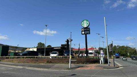 An image of a Starbucks drive-thru on the corner of a main road with a tall sign outside. 