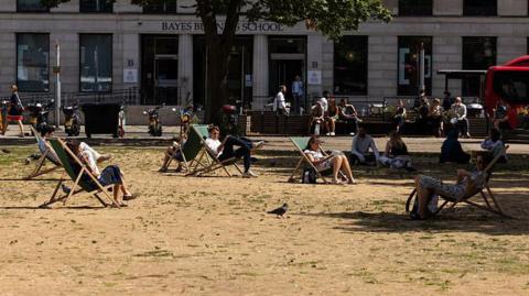 People sit on seats surrounded by dry grass in London.