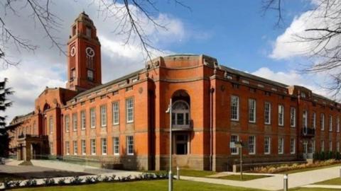 A view of red brick Trafford Town Hall with lawns and shrubs surrounding it.