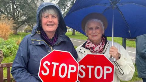 A picture of two ladies holding a sign each. It is red signs with the word STOP on it.