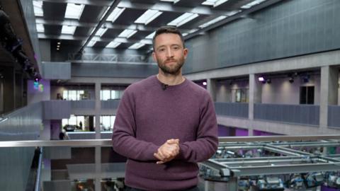 David Wallace Lockhart in BBC office in Scotland looking down the lens dressed in a purple jumper