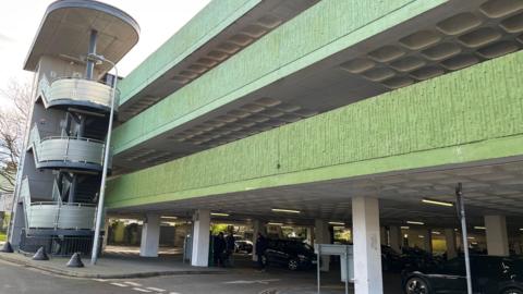 The exterior of the Tenby car park, with three storeys visible and cars inside, and the entrance road 