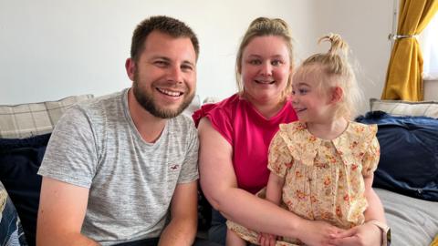 Jodie, Rich and Amelia sitting on a sofa at home smiling at the camera