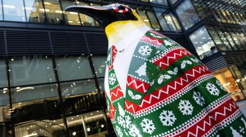 Penguin statue in green and red festive suit with snowflakes and Christmas trees