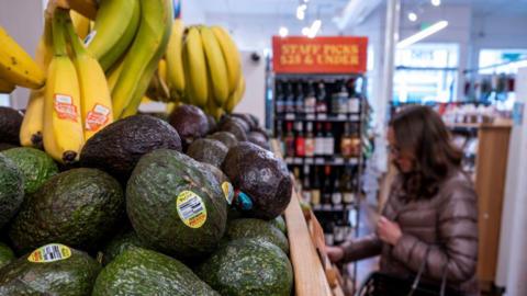 Avocados and bananas at grocery store in San Francisco, California, US, with someone in a puffer coat in the background