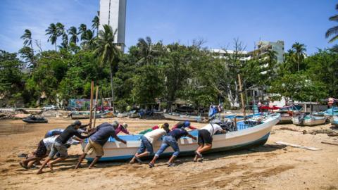 People push a boat up a sandy beach to secure it ahead of Hurricane Erick