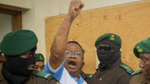 Tanzania's main opposition leader Tundu Lissu (2nd L) raises his fist in the air as he enters the court room at Kisutu magistrate's court in Dar es Salaam. He is surrounded by security officers in uniform, some with face masks