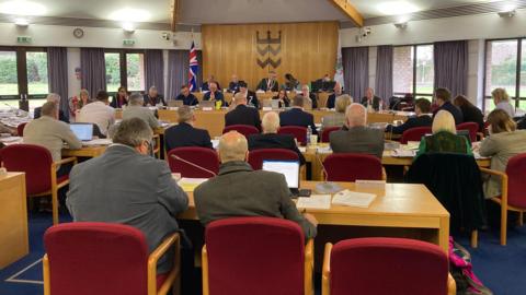 A group of men and women sat inside a council chamber, as the meeting to agree the council tax levy takes place.
