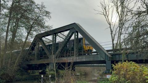 A green GWR train travels over the Shalford bridge over the River Wey