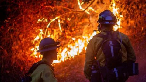 Firefighters with gas masks look on as wildfire blaze burns in background