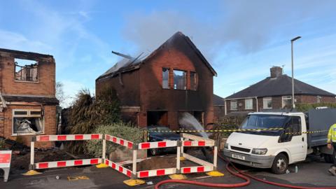 A house that has been destroyed by a fire. All that remains is a shell of brick work, charred timber, rubble and ash.