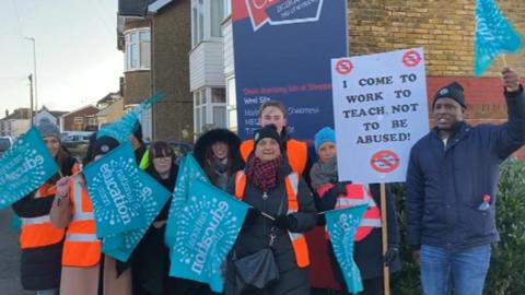 A group of teachers waving National Education Union flags and a banner that reads: "I come to work to teach, not to be abused!"