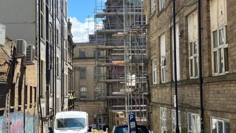 A view of a street with tall brick buildings and a building surrounded by metal scaffolding at the end of the road.