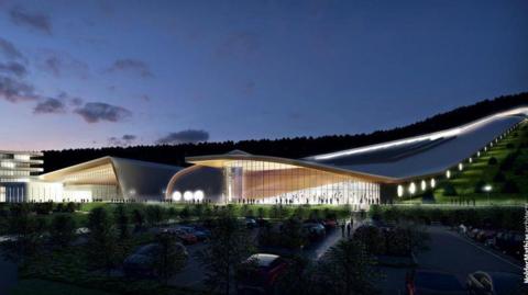 An artist's impression of how the plans might look. A long futuristic building with a rounded glass front stretches up a steep hillside with round windows running alongside the walls. There is another large building with a glass front to its left, with a large car park with shrubs between vehicles in front of the two. 