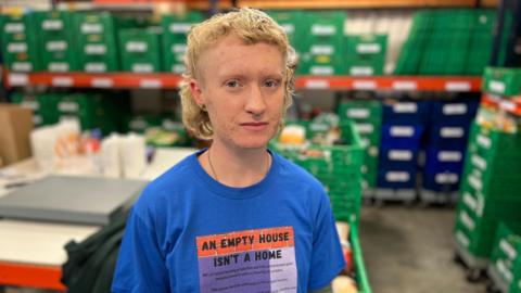 A person with blond hair wearing a blue t-shirt in front of green trays