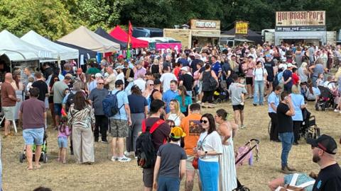 Large crowds of people gathered at the open day event. There are numerous stalls in the background. 