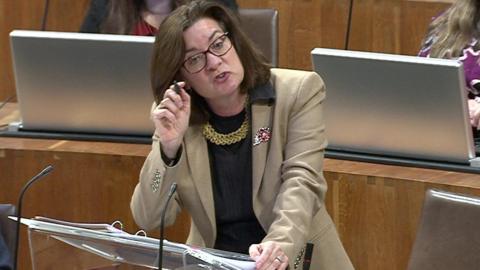 Eluned Morgan on her feet answering First Minister's Questions on Tuesday. She is holding a pen and pointing at the Conservative leader in the Welsh Parliament, Andrew RT Davies, who is out of shot. Morgan is wearing spectacles and a cream coloured jacket