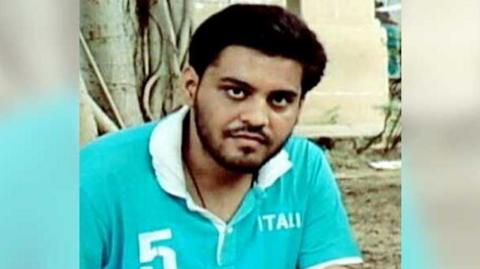 Najeeb Ahmed wearing a blue coloured t-shirt with white collars sitting in a park 