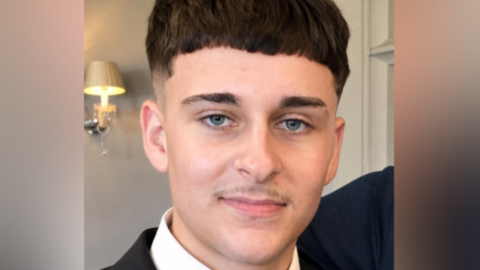 A picture of Muhammad Noor Majid Butt, who is wearing a white shirt and black jacket. He has brown hair and a moustache. 