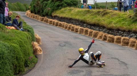 A skateboarder wearing a yellow helmet negotiates a sharp right-handed bend.