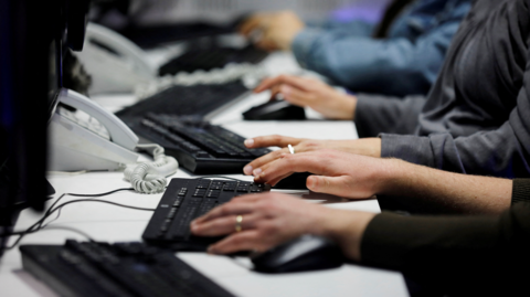 Employees at a row of desks typing on keyboards.