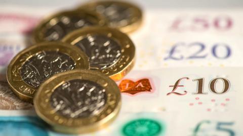 Five £1 coins loosely piled on top of a range of fanned bank notes from lowest to highest value with the £10 note being in focus