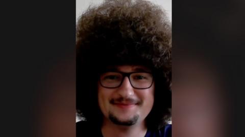 Manchester United fan Frank Ilett has large curly dark hair, bigger than his face, and is wearing glasses