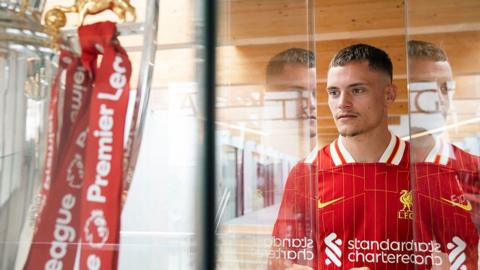 Florian Wirtz gazes at the Premier League trophy while wearing a Liverpool kit