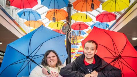 Two children stood in front of the multi-coloured umbrellas making up the art display.