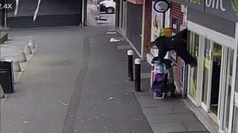 Woman mid-air, attached by coat to shop shutters.