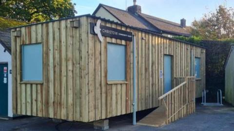 The shop is a rectangle with wooden panels all across it, with three windows and a door.