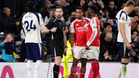 Assistant referee Blake Antrobus explains the problem to the Tottenham and Arsenal players