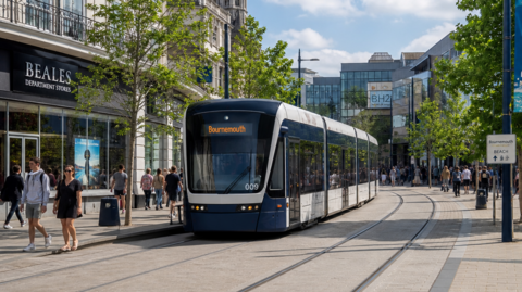 A computer-generated image of a tram making its way through a town centre. The tram has an electronic sign reading "Bournemouth" on the front and is travelling along a track that curves past the view of the camera. People can be seen walking around in the area surrounding the tram.
