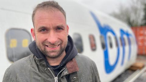 Man in a waterproof jacket in front of a white plane fuselage