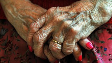 A close-up of an elderly woman's wrinkled hands with red painted nails.