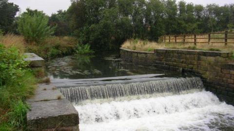 River Irk surrounded by trees and walls - a wooden fence on the right