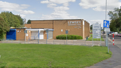 The outside of Lewsey Swimming Pool, with a sign advertising sports available at Lewsey Sports Park