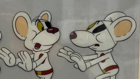 Cartoon strip shows two depictions of Danger Mouse - a cartoon white mouse with a blindfold over his left eye. Both versions have their hands stretched out in front of them as they look towards each other.