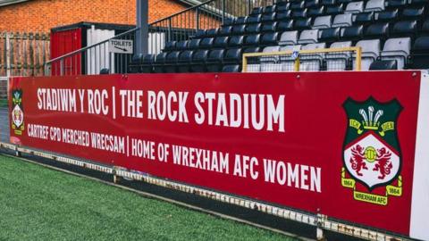 Picture of a stand at the Rock and a sign saying it is the home of Wrexham Women