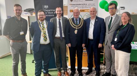 Six men and a woman stand in a semi circle smiling at the camera