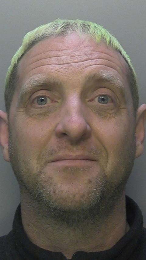 A police mugshot of a man with green hair.