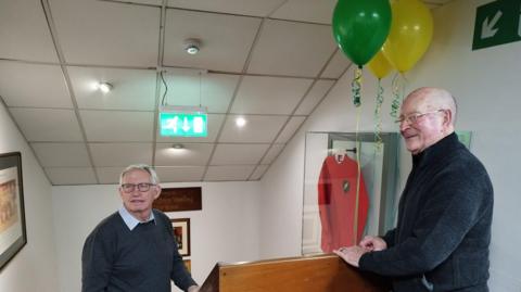 Former Norwich City players Clive Payne and Dave Stringer standing by the shirt worn by Duncan Forbes