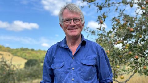 Farmer Ian Boyd wears a blue shirt in front of an apple tree in a field