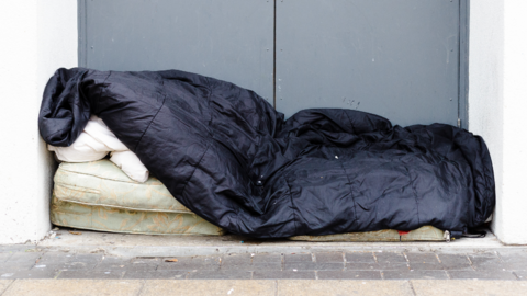 Stark image of a black sleeping wag on top of a dirty mattress, in a doorway, against a grey wall