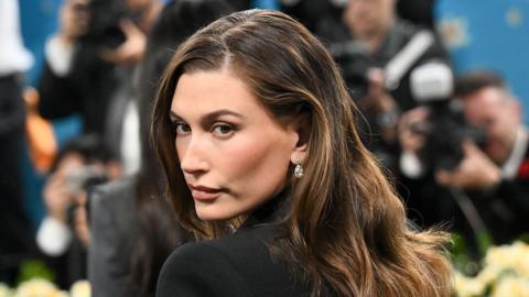 Hailey Bieber at The 2025 Met Gala. She is wearing a black dress with earrings. 