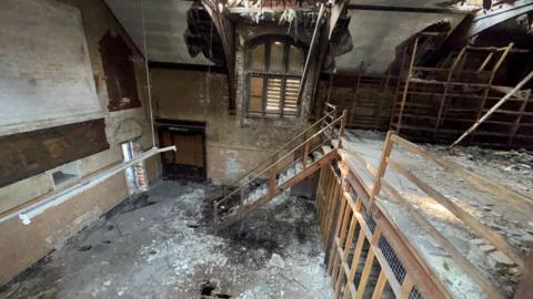 Dilapidated inside of an old building with wooden stairs and rubble on the ground