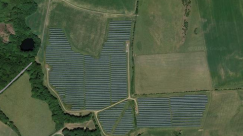 A view from above of the current solar farm in Roanhead. There are a number of green fields and an area of woodland. Across the middle of the image are many rows of solar panels covering three fields.