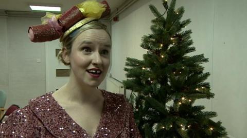 Sarah Boulter in costume wearing a hat. A Christmas tree is behind her.