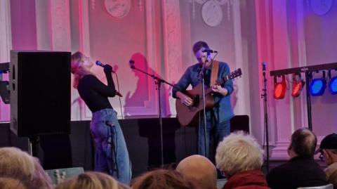 Two musicians performing on a stage with a crowd in front of them