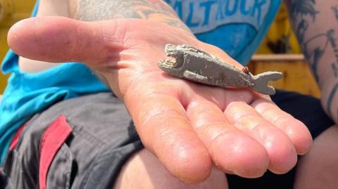 Richard West's open hand in which lies the sea-worn grey Lego shark. It looks worn but has a clear outline of a shark.